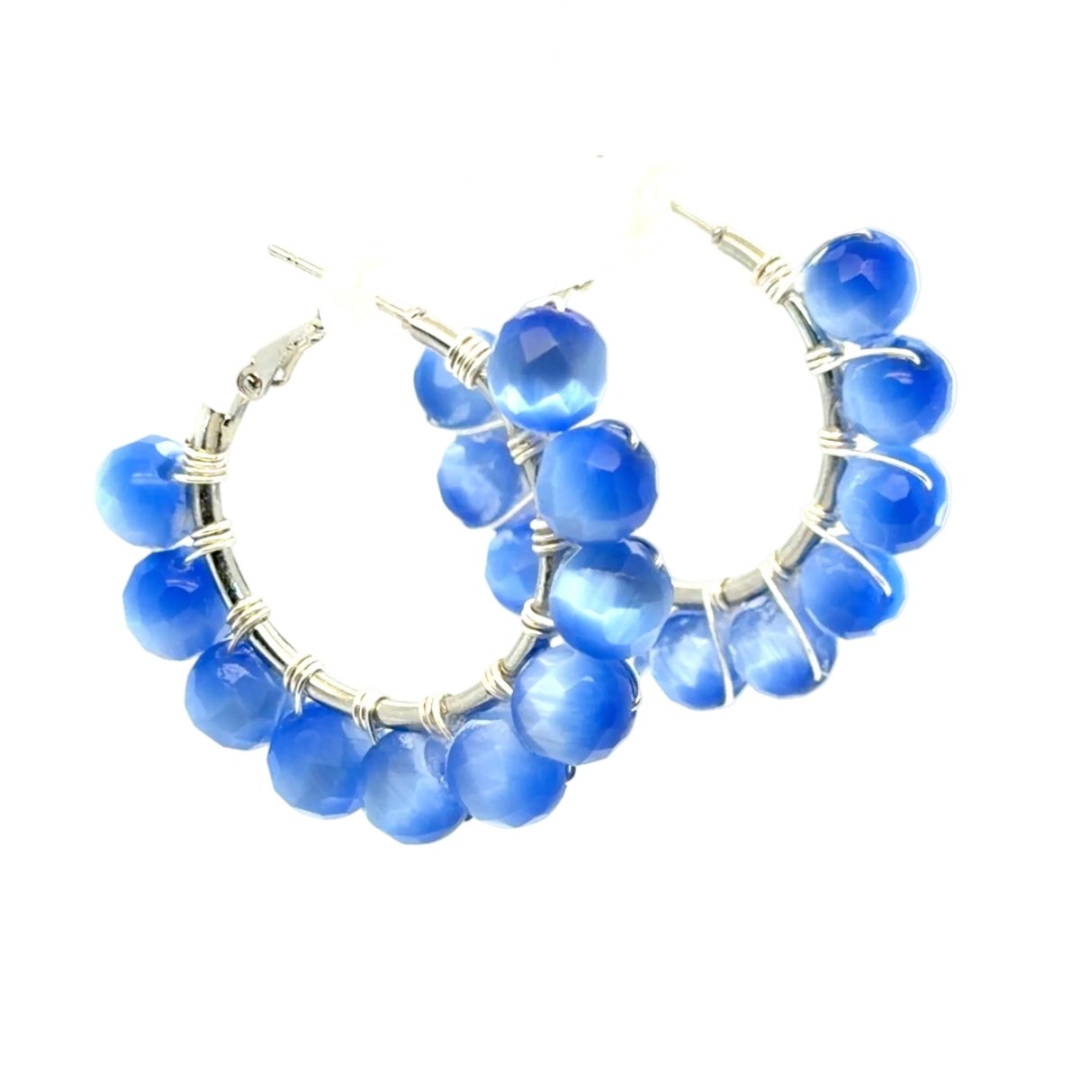 A pair of silver hoop earrings adorned with multiple faceted blue beads wrapped in silver wire, shown against a plain white background.