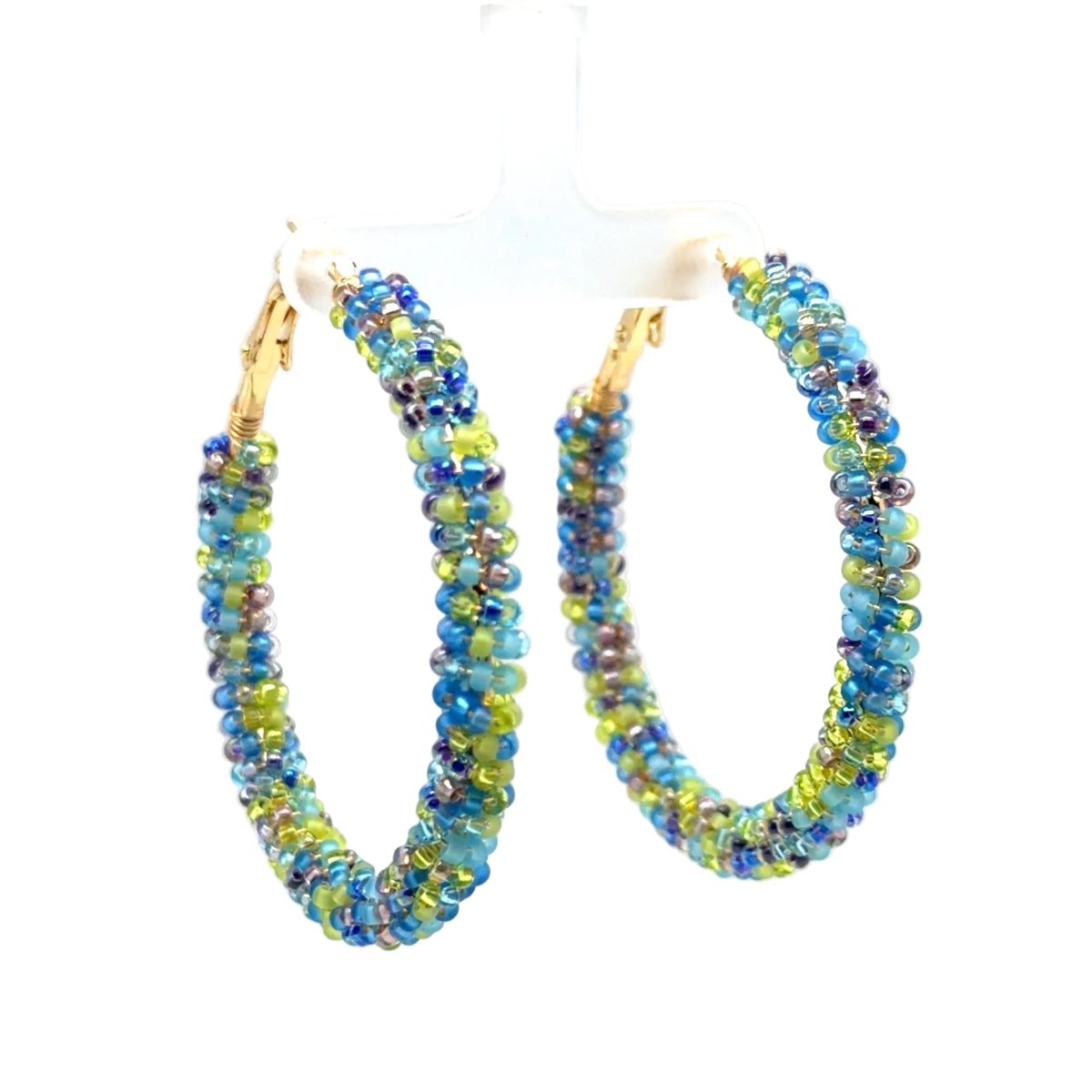 A pair of large hoop earrings made of small faceted beads in blue, green, and purple tones, with gold-tone hooks, displayed on a white plastic hanger against a white background.