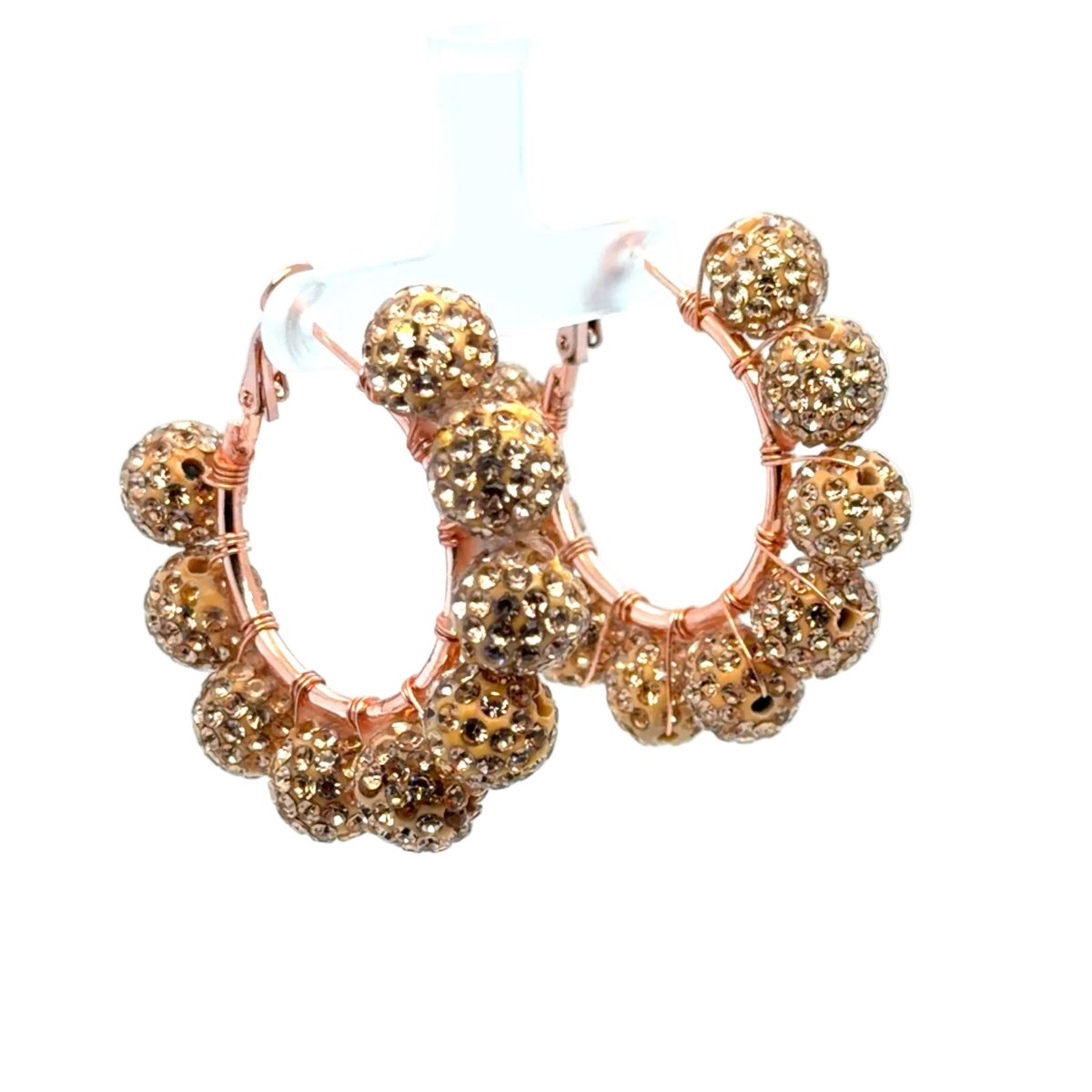 Rose gold hoop earrings adorned with multiple faceted gold rhinestone-covered beads, displayed on a white plastic stand against a white background.