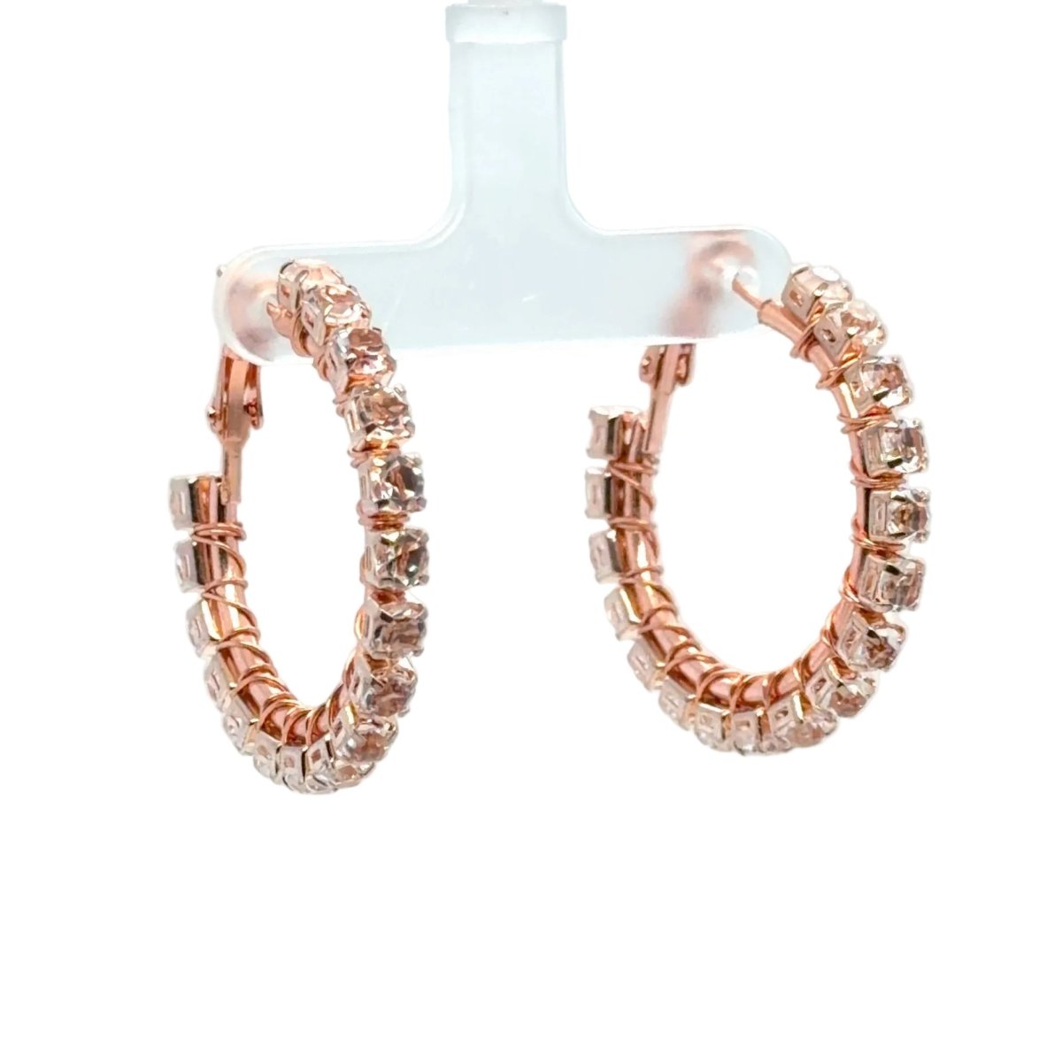 Rose gold hoop earrings adorned with clear rhinestones, displayed on a translucent plastic T-stand against a white background.
