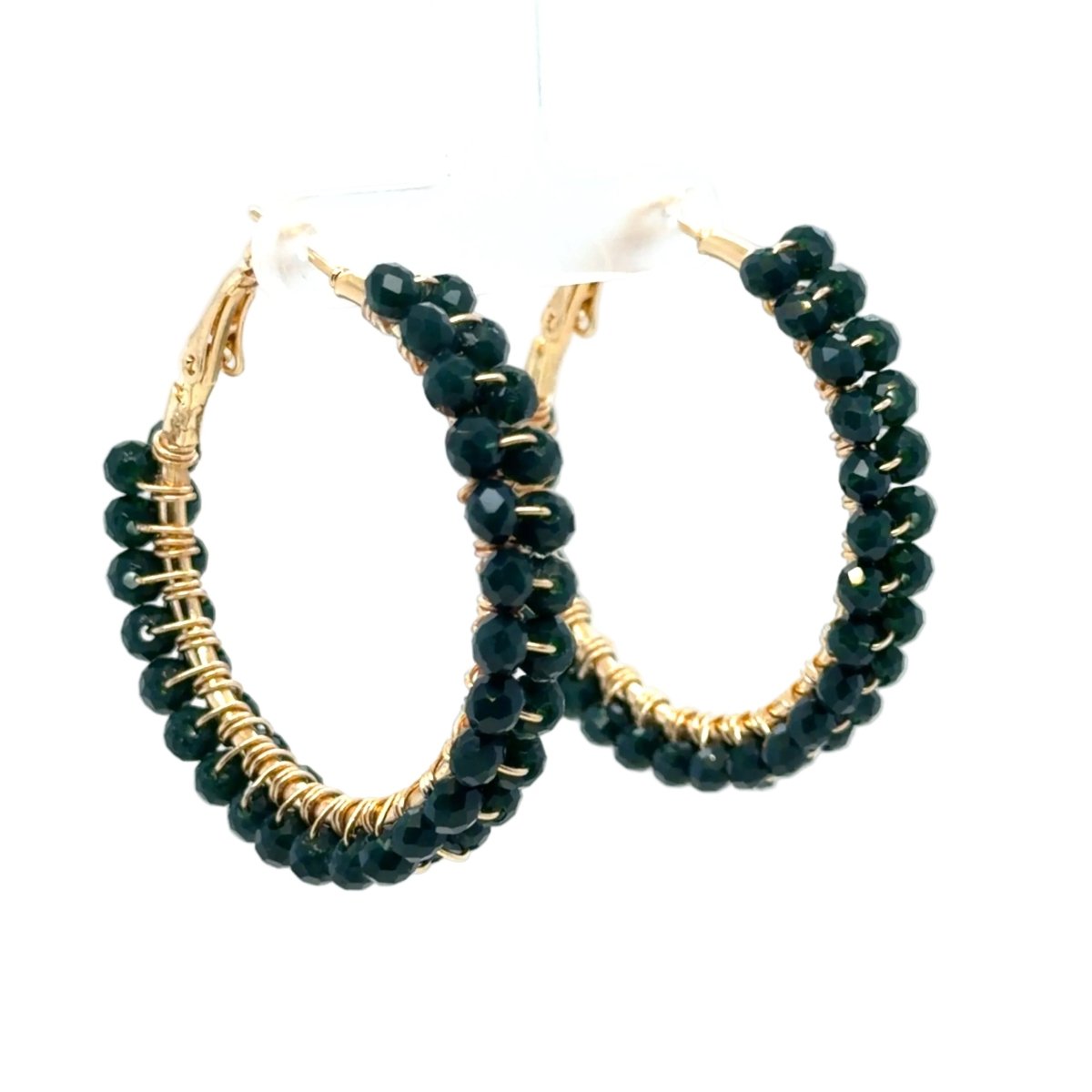 Gold hoop earrings with faceted dark green beads, displayed on a white plastic stand against a white background.
