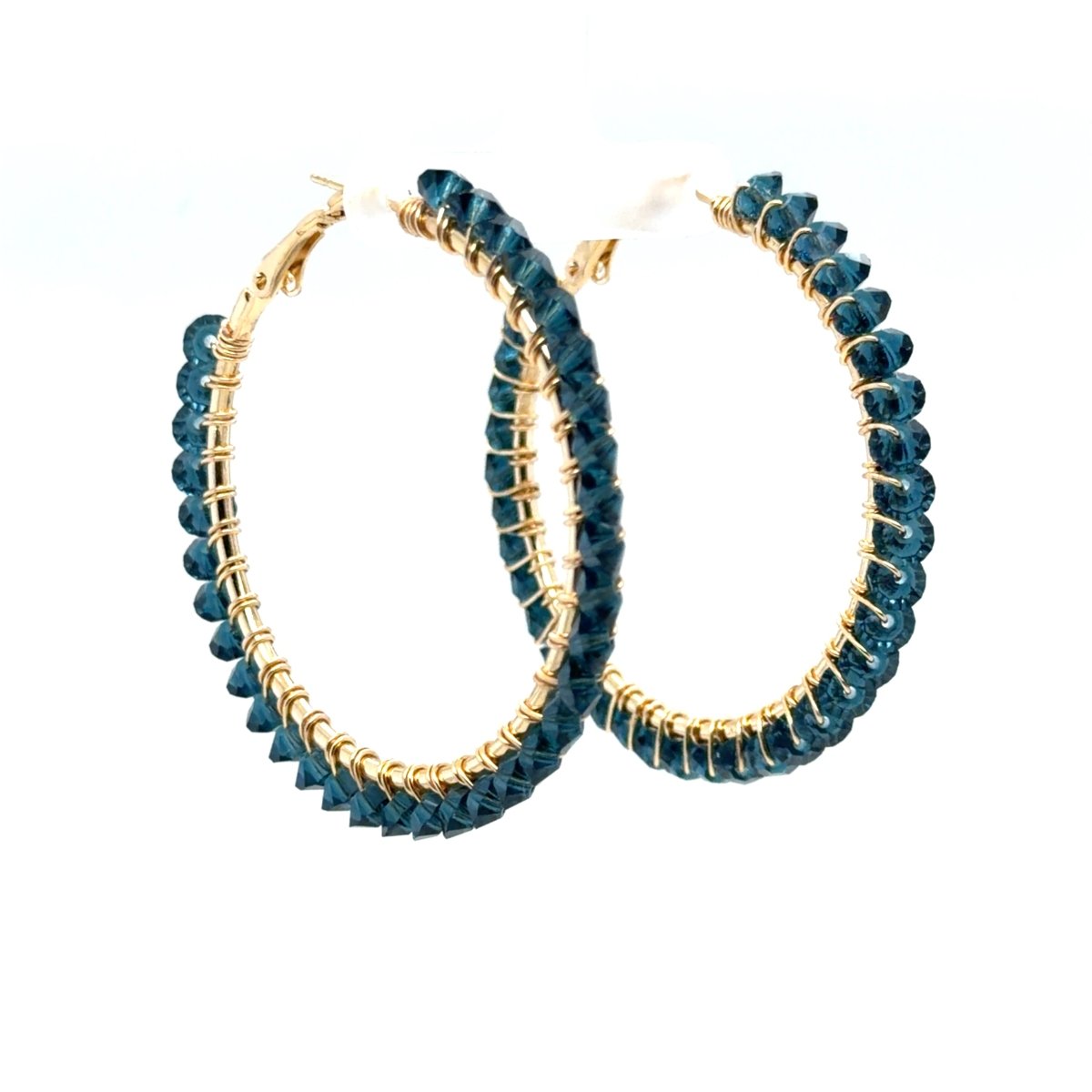 Maeven in Me denim blue beaded gold hoop earrings shown at an angle on a white display stand.