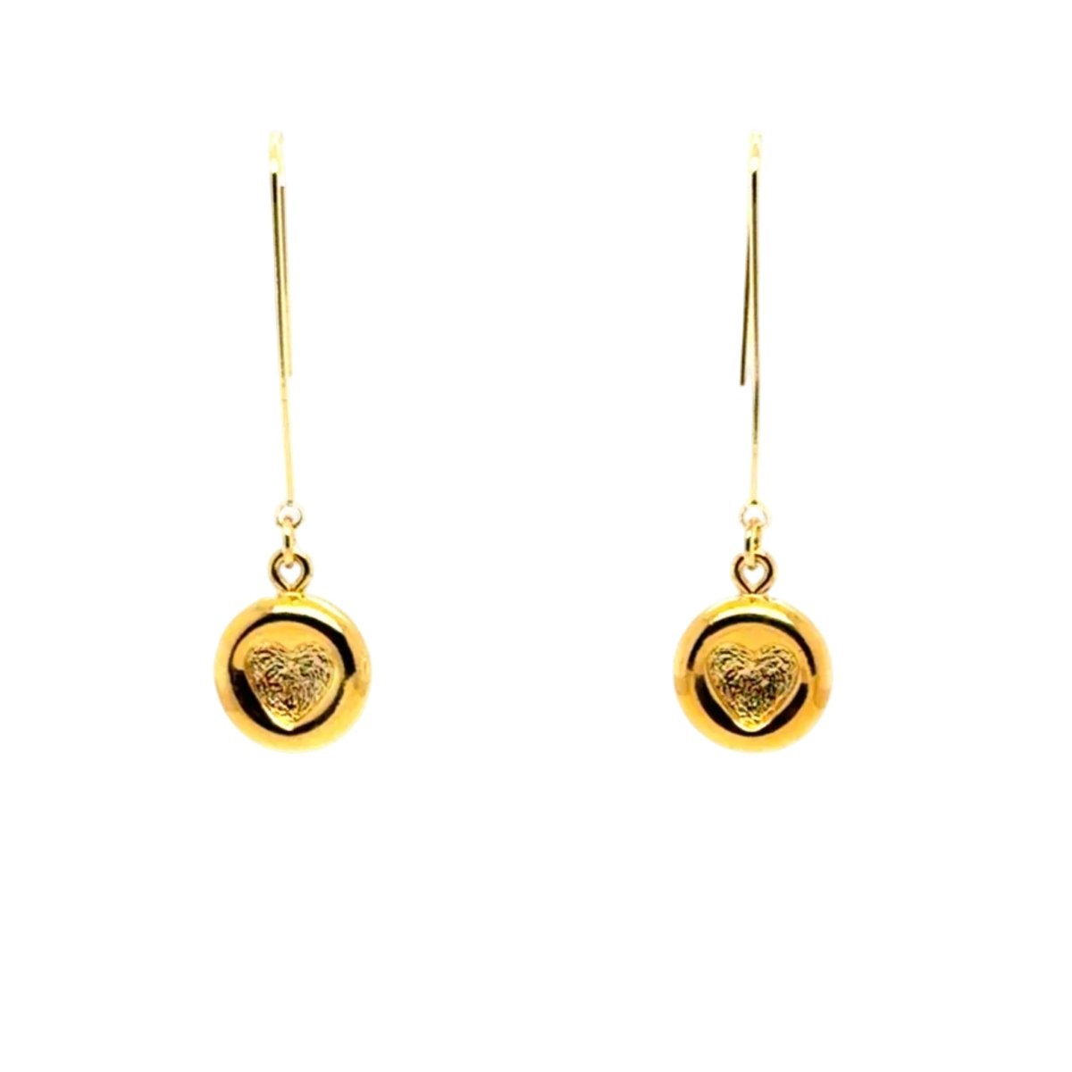 A pair of gold drop earrings with a circular disc pendant featuring an engraved heart design, suspended from thin wire hooks on a plain white background.