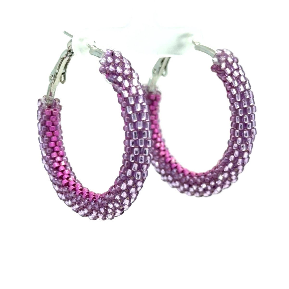 A pair of large hoop earrings made from tightly woven seed beads in shades of pink and purple, with silver-toned metal hooks, shown against a plain white background.