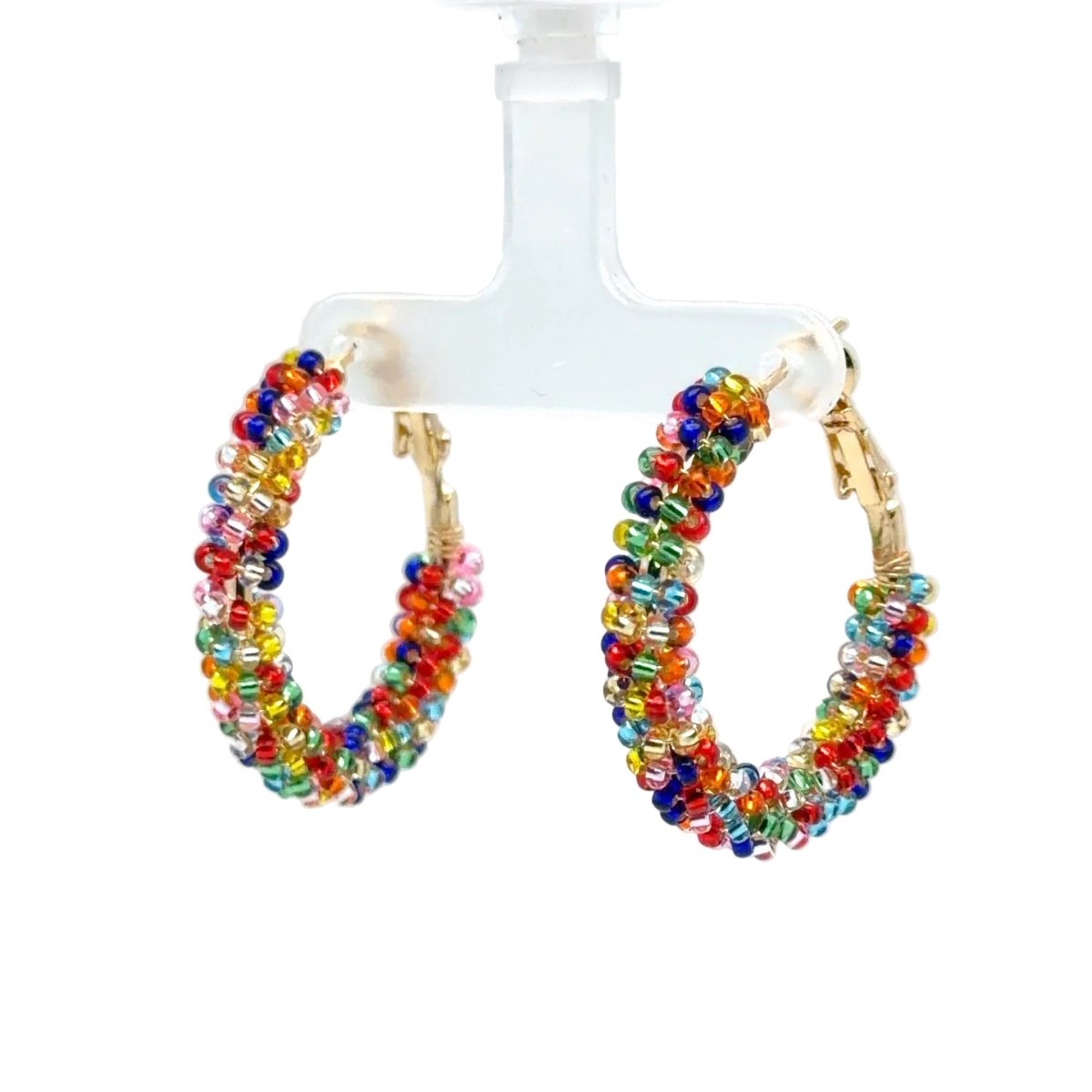 A pair of large gold hoop earrings wrapped in multicolor seed beads, hanging from a clear plastic display stand against a white background.