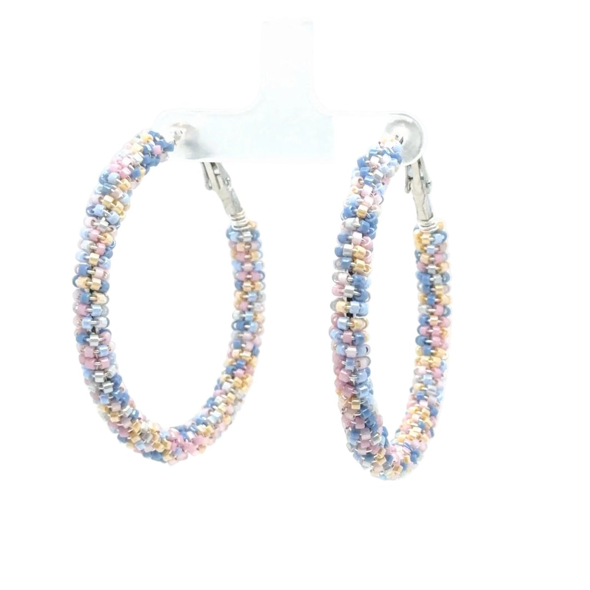 A pair of large hoop earrings made from tightly woven iridescent beads in pastel shades of blue, pink, yellow, and white, hanging from silver-toned posts on a clear display stand against a white background.