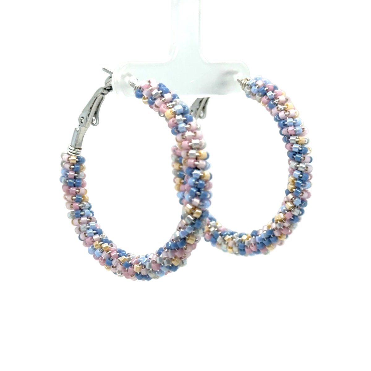A pair of large silver hoop earrings adorned with small, iridescent seed beads in pastel shades of blue, pink, and gold, displayed on a clear plastic stand against a white background.