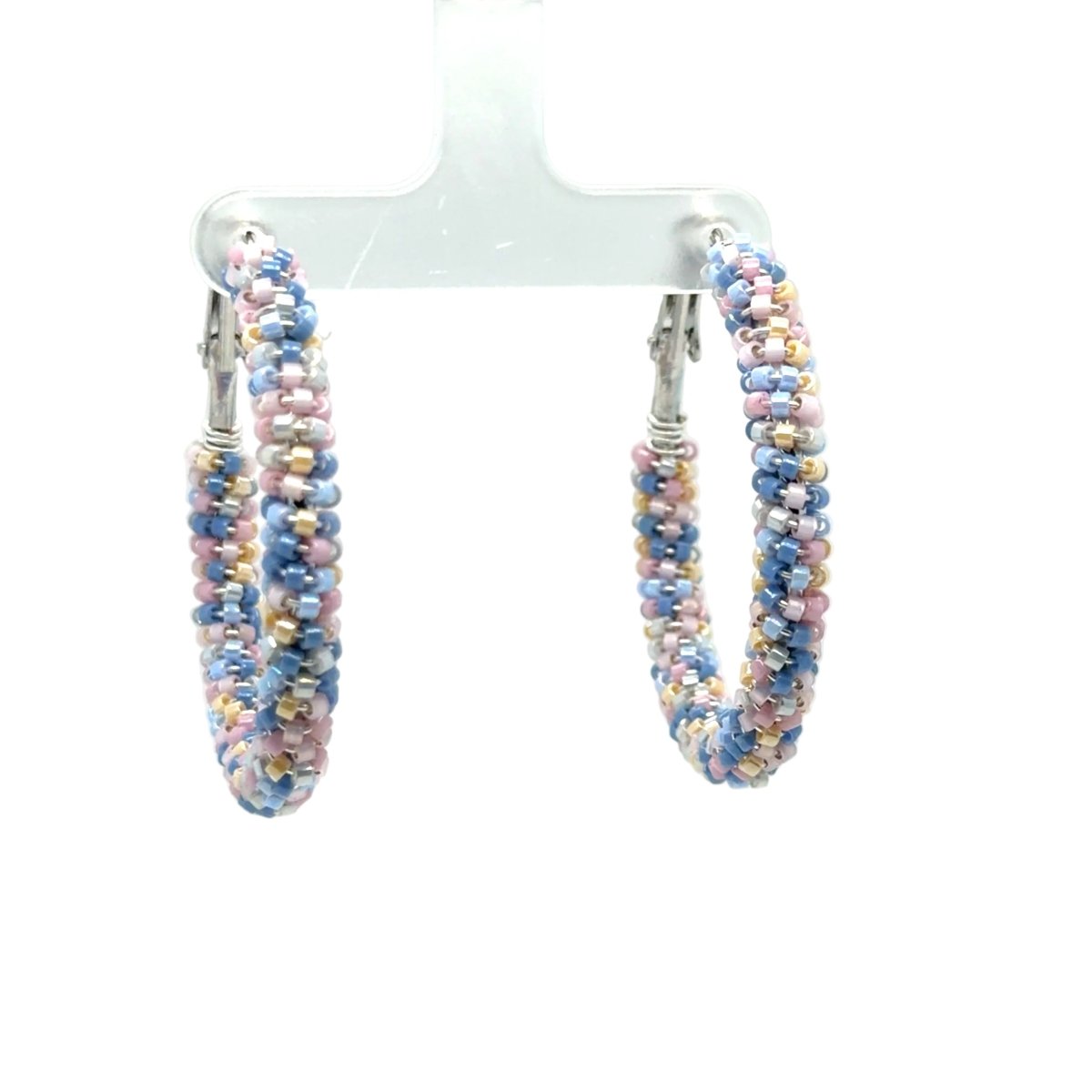A pair of handmade beaded hoop earrings with blue, pink, and gold seed beads, hanging from a clear plastic display stand against a white background.