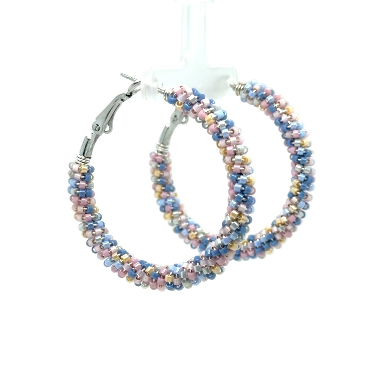 A pair of large hoop earrings made from small multicolored beads in shades of blue, pink, and gold, with silver-tone clasp closures, displayed on a clear stand against a white background.