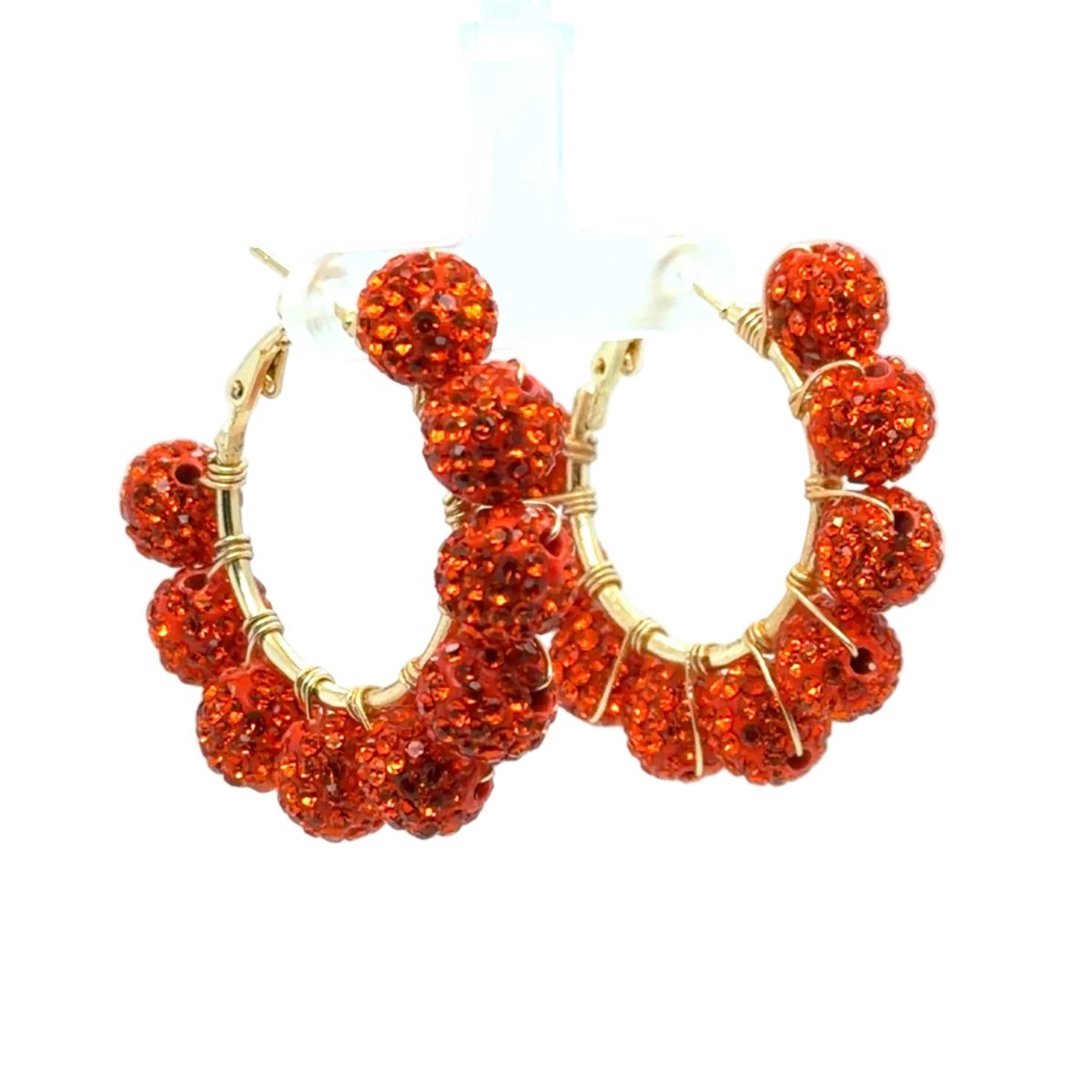 A pair of gold hoop earrings adorned with multiple round, textured red-orange rhinestone clusters, displayed against a clean white background.