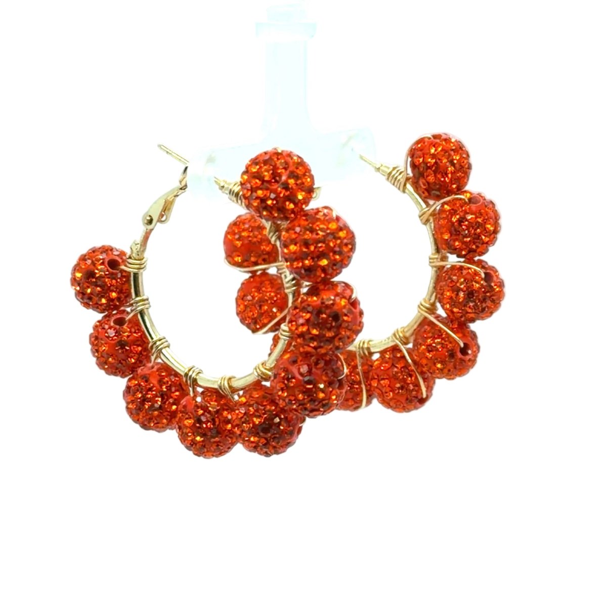 A pair of gold hoop earrings adorned with multiple round, orange-red glittery beads, displayed against a clean white background.