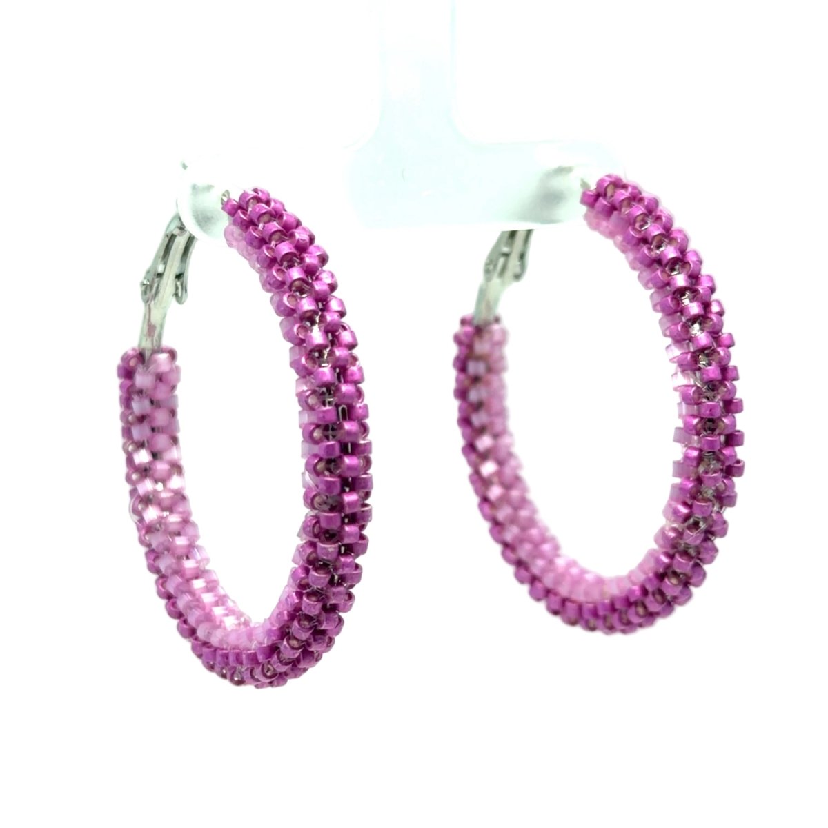 A pair of large hoop earrings covered in small faceted pink beads, hanging from silver-tone clips on a white display stand against a light green-to-white gradient background.